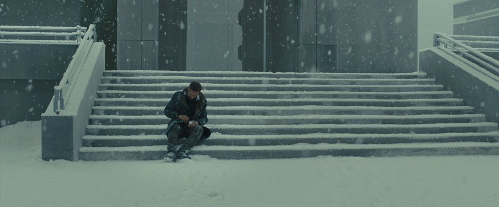 Plan du film Blade Runner 2049 de Denis Villeneuve (2017) : l'agent K assis seul sur des marches enneigées.